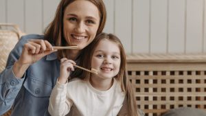 A Woman and a Child Smiling While Holding a Wooden Toothbrush